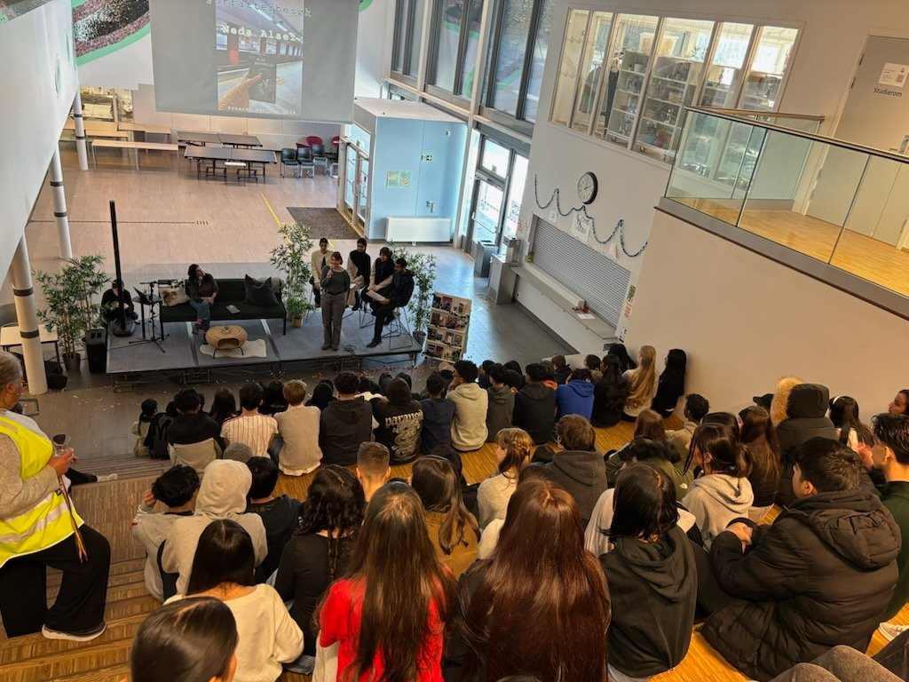 en gruppe mennesker som sitter i et rom med en scene og en stor gruppe mennesker